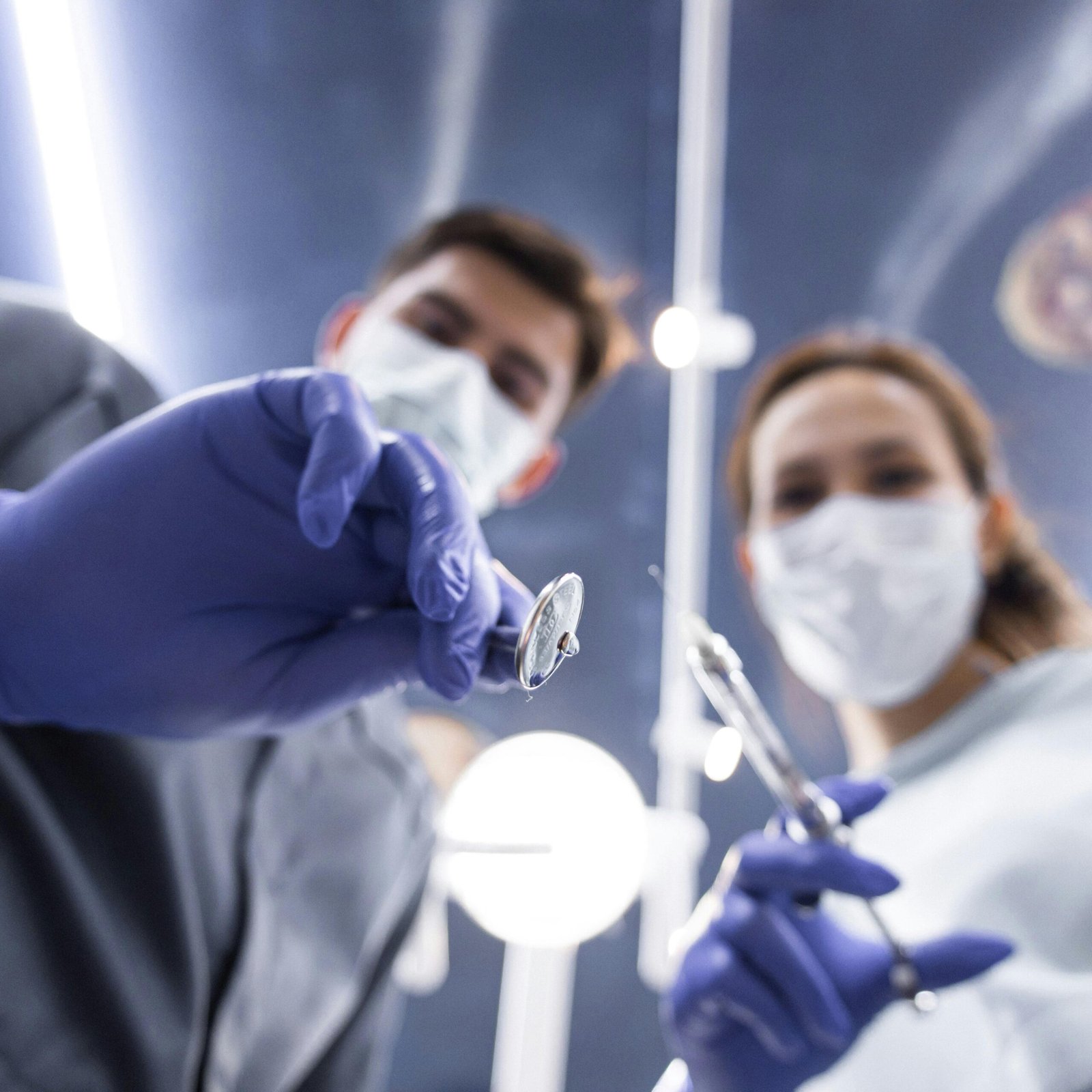 Two dentists in masks and gloves holding dental tools from a low angle view.